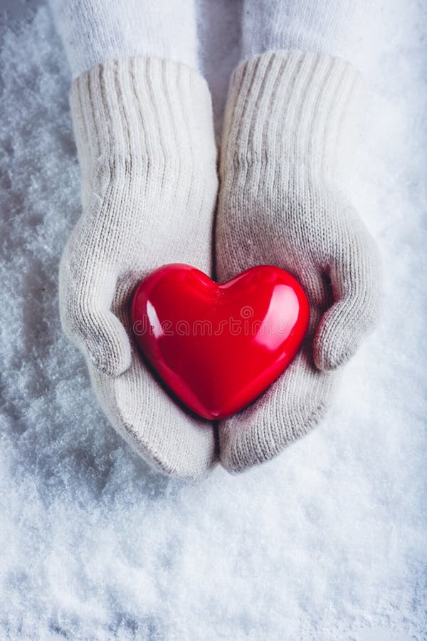 Het wijfje dient witte gebreide vuisthandschoenen met een glanzend rood hart op een sneeuwachtergrond in Liefde en St Valentine c royalty-vrije stock foto Het wijfje dient witte gebreide vuisthandschoenen met een glanzend rood hart op een sneeuwachtergrond in Liefde en St Valentine c royalty-vrije stock foto