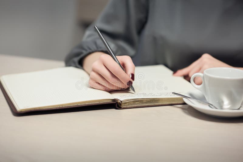 Het wijfje heeft koffiepauze en het schrijven nota's in agenda of blocnote; stock foto Het wijfje heeft koffiepauze en het schrijven nota's in agenda of blocnote; stock foto