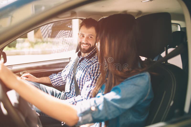 Het zorgvuldige drijven Mooie jonge paarzitting op de voorpassagierszetels en het glimlachen terwijl vrouw die een auto drijven