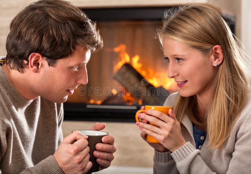 A couple warming up with hot drinks by a fireplace. A couple warming up with hot drinks by a fireplace