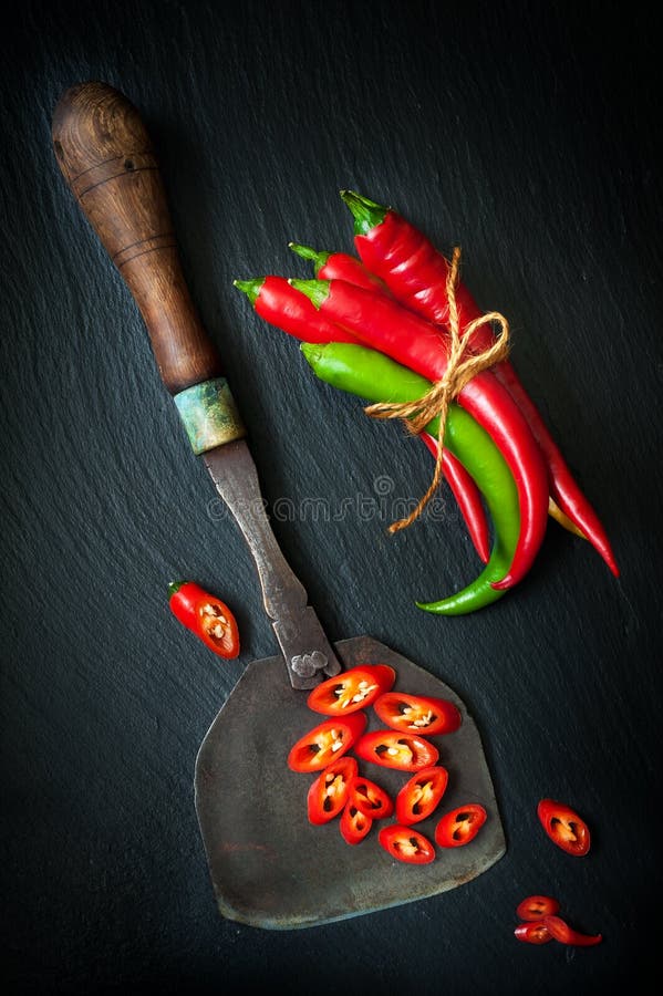 Hete Spaanse peperpeper en uitstekend mes voor het hakken van kruiden op een leibord royalty-vrije stock foto Hete Spaanse peperpeper en uitstekend mes voor het hakken van kruiden op een leibord royalty-vrije stock foto