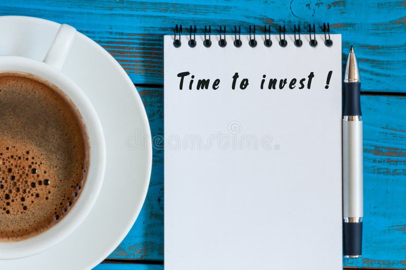 Heure d'investir - l'avis en bloc-notes à la table en bois bleue avec la tasse de café de matin L'épargne, concept d'affaires d'a photographie stock Heure d'investir - l'avis en bloc-notes à la table en bois bleue avec la tasse de café de matin L'épargne, concept d'affaires d'a photographie stock