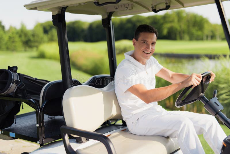 Heure pour un jeu du golf Un homme dans un costume blanc monte un chariot de golf blanc image libre de droits Heure pour un jeu du golf Un homme dans un costume blanc monte un chariot de golf blanc image libre de droits