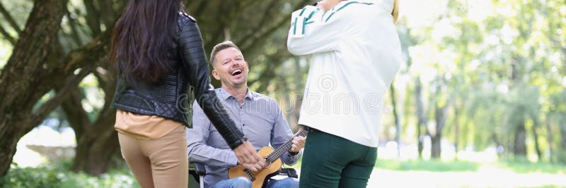 Heureux défunt homme en fauteuil roulant jouant ukulele pour ses amis dans le parc. photos libres de droits
