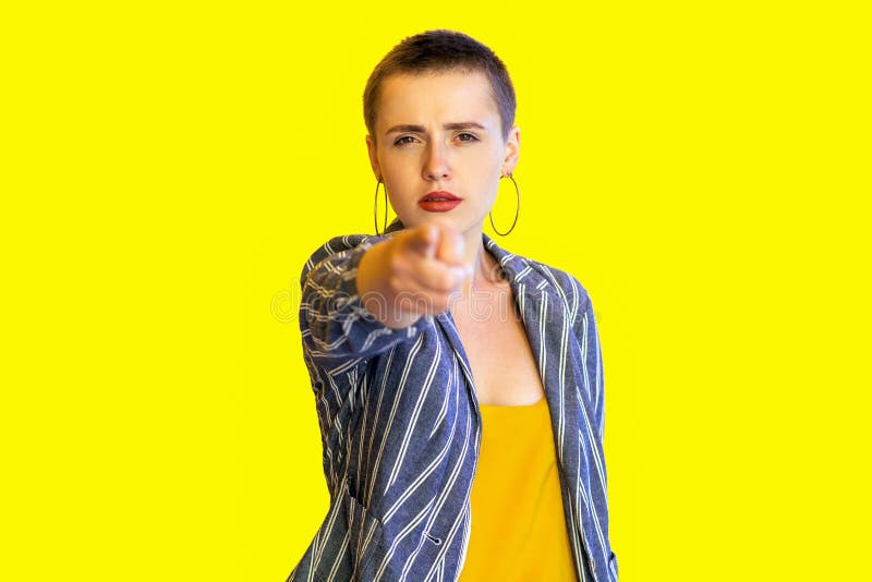 Hey you. Portrait of serious young short hair beautiful woman in yellow shirt and striped suit standing, looking and pointing at stock images Hey you. Portrait of serious young short hair beautiful woman in yellow shirt and striped suit standing, looking and pointing at stock images