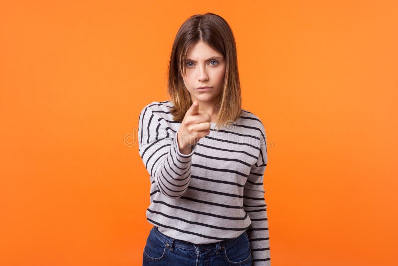 Hey you! Portrait of suspicious disgruntled young woman with brown hair in long sleeve striped shirt. indoor studio shot isolated