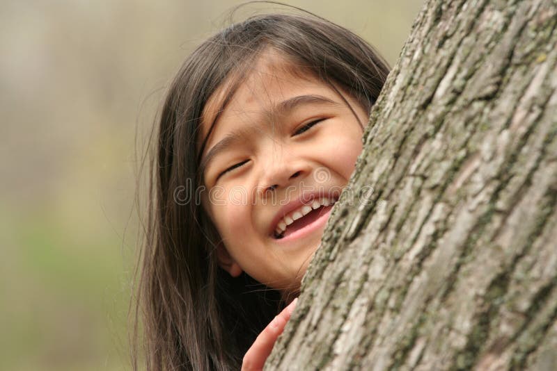 Little girl peeking out from behind a tree. Little girl peeking out from behind a tree