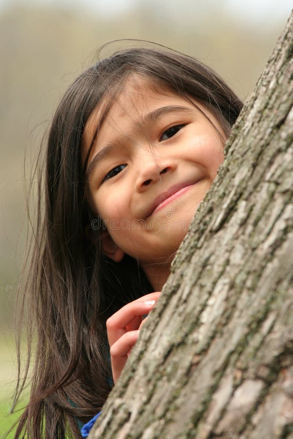 Little girl peeking out from behind a tree. Little girl peeking out from behind a tree