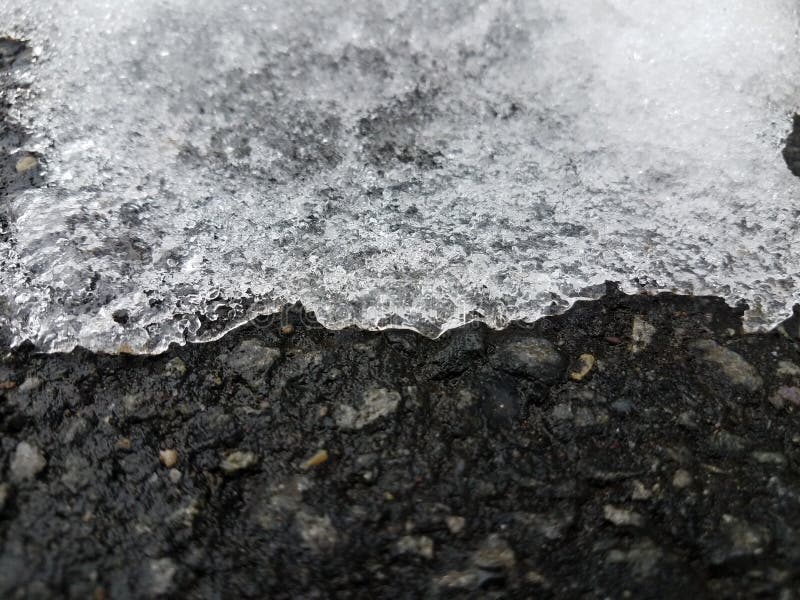 Hielo que derrite en el asfalto o el pavimento negro imagen de archivo libre de regalías Hielo que derrite en el asfalto o el pavimento negro imagen de archivo libre de regalías