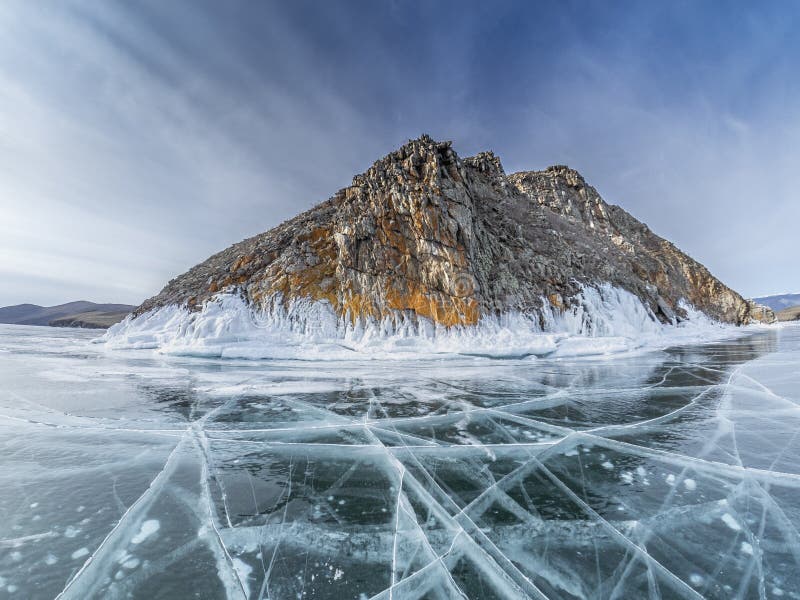 Hielo transparente con las grietas y las grietas en el lago Baikal cerca del acantilado congelado con las piedras cubiertas por l imagenes de archivo Hielo transparente con las grietas y las grietas en el lago Baikal cerca del acantilado congelado con las piedras cubiertas por l imagenes de archivo
