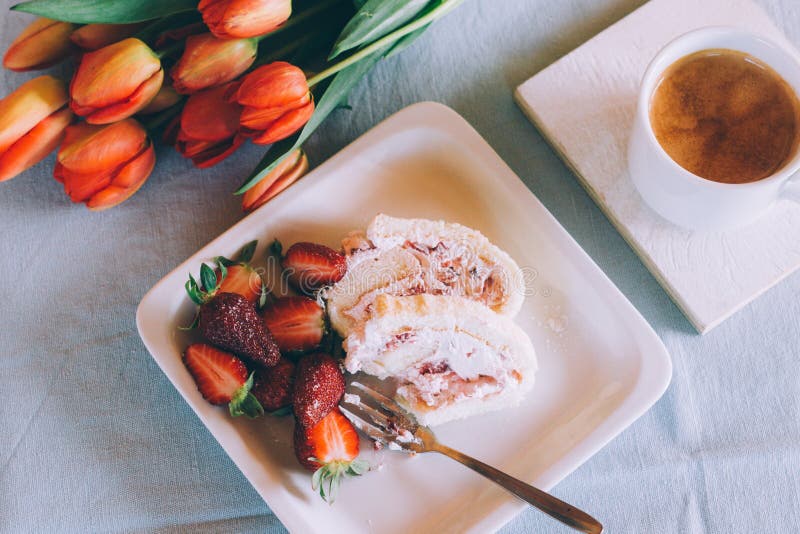 High angle closeup shot of a delicious strawberry dessert and a cup of coffee next to orange tulips.