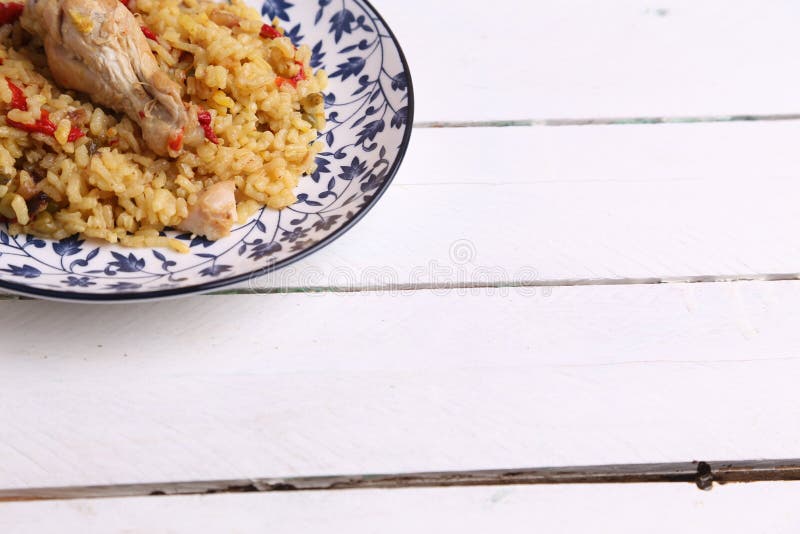 High angle shit of cooked rice and chicken on a white and blue plate placed on a wooden table stock image