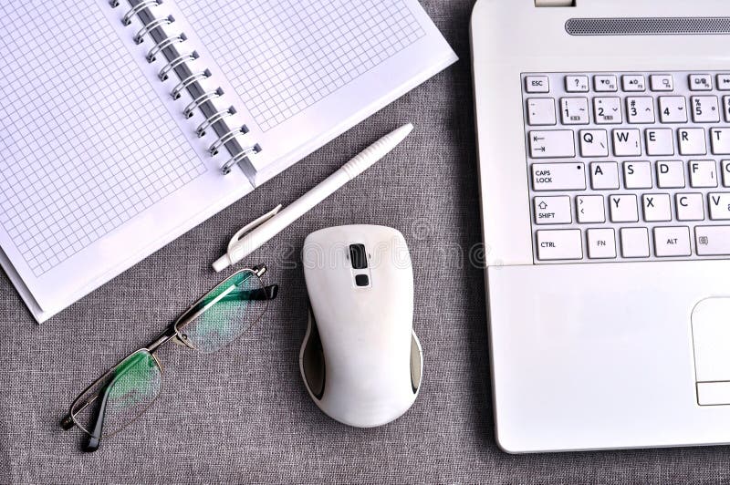 High angle view of office workplace with tablet and laptop close up computer keyboard and mouse with paper, pen and eyeglasses on grey desk. Working desk table concept.