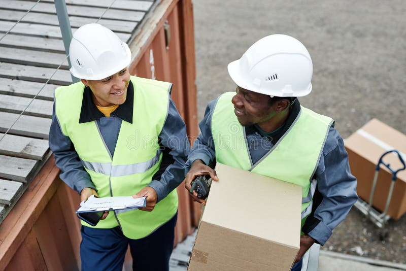 Two smiling workers carrying boxes at shipping docks