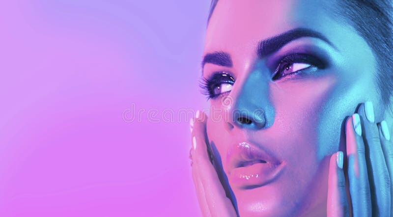 High Fashion model girl face in colorful bright UV lights in studio, portrait of beautiful woman with trendy make-up and manicure