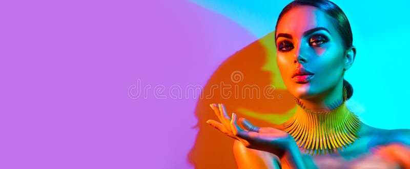 High Fashion model woman portrait in colourful bright neon lights, beautiful party girl with trendy make-up, manicure, hairstyle. Pointing hand, advertising gesture over colorful vivid background