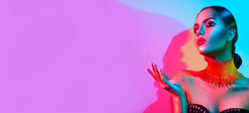 High Fashion model woman portrait in colourful bright neon lights, beautiful party girl with trendy make-up, manicure, hairstyle. Pointing hand, advertising gesture over colorful vivid background