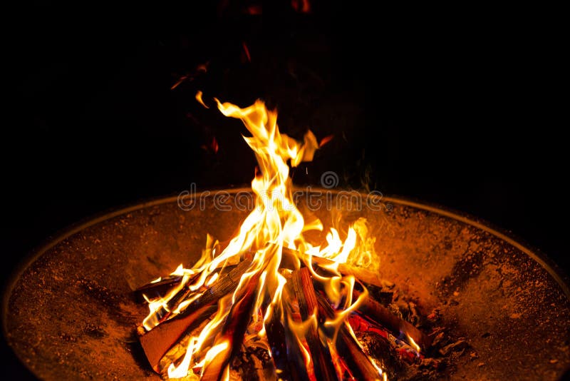 High flames from a burning wood fire on a metal grate at night.