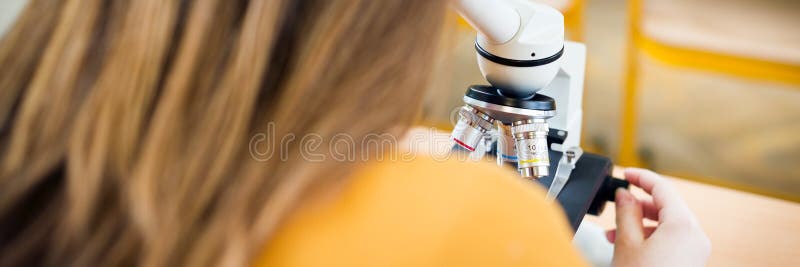 High School female student in biology class. Student using microscope.