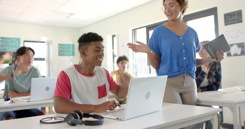 In high school, students raising hands and using laptops in classroom with teacher stock video footage