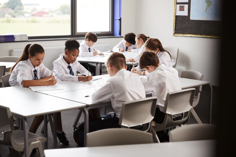 High School Students Wearing Uniform Sitting And Working Around Table In Lesson