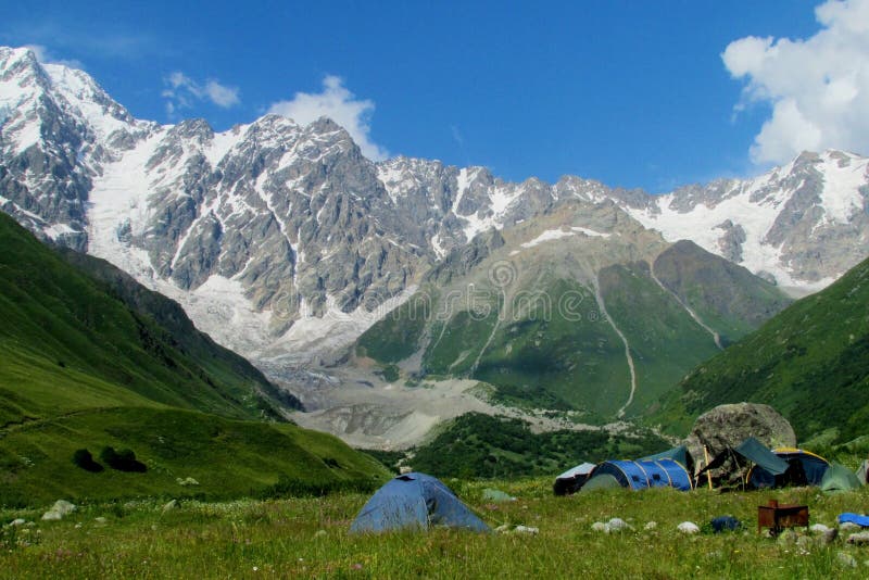 High snow mountain range above camping tents in green valley