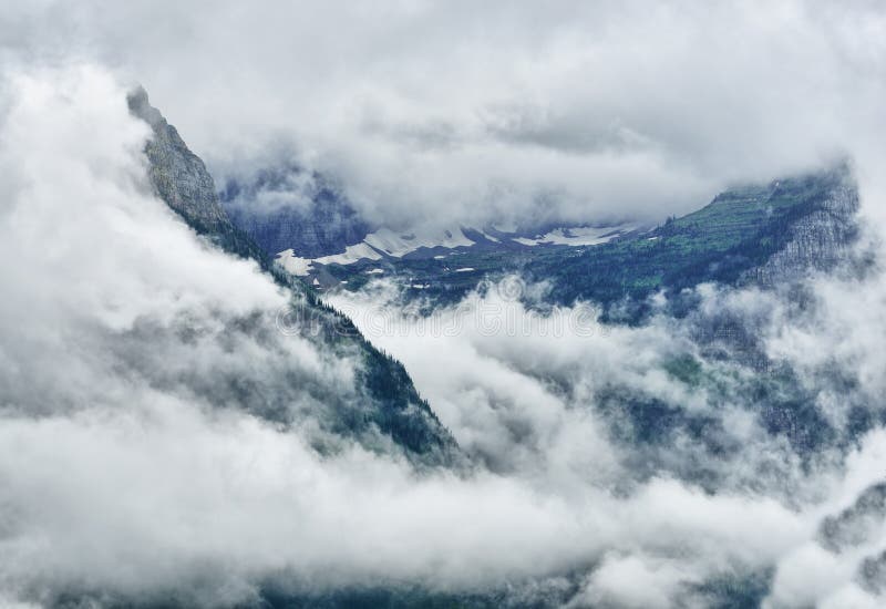 High and steep mountain surrounded by heavy clouds stock photo