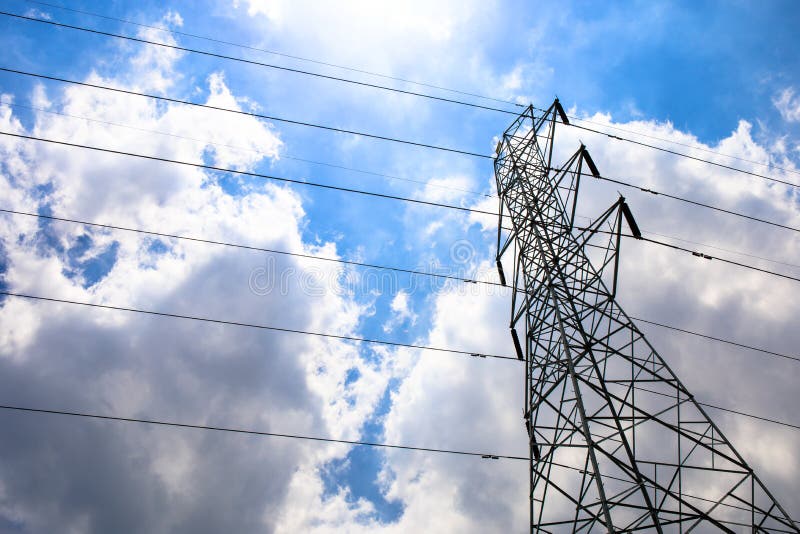 High voltage tower electric pole and wire with blue sky clouds and sun light.