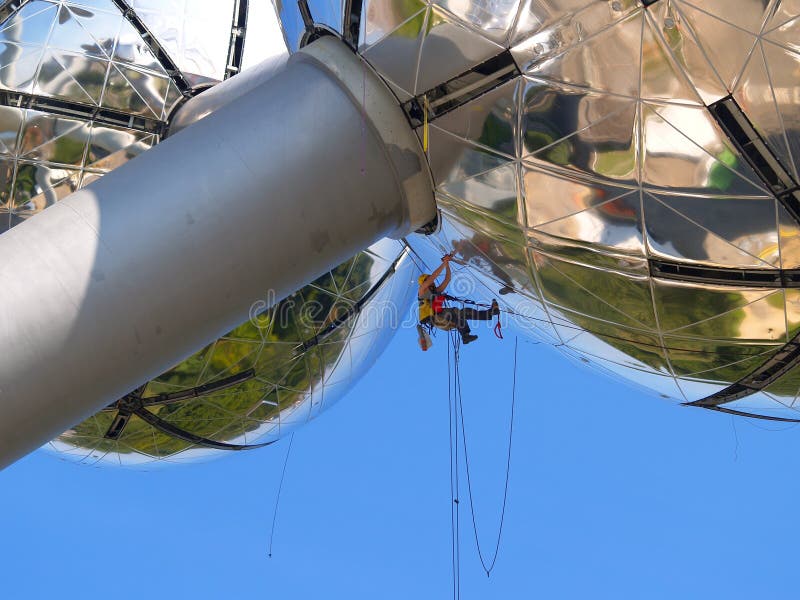 High-rise construction worker suspended on steel cables working on a modern and daring spherical steel building. High-rise construction worker suspended on steel cables working on a modern and daring spherical steel building.