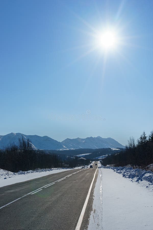 Highway to the mountain among snow and ice at winter time ander blue sky with sun