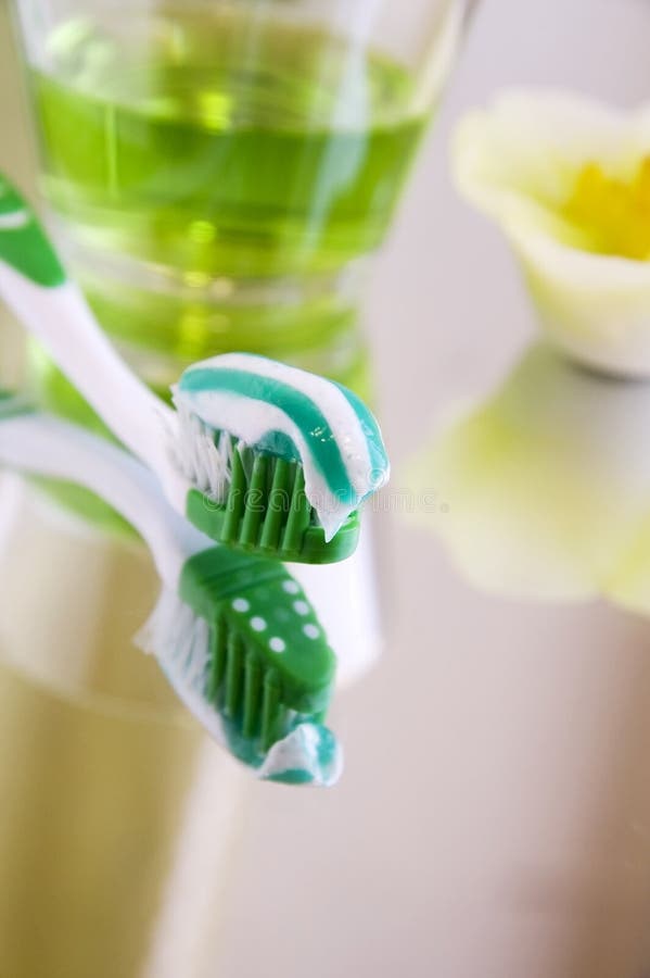 Oral hygiene products - a tooth-brush with toothpaste and rinsing liquid on a mirror surface, close up, vertical. Oral hygiene products - a tooth-brush with toothpaste and rinsing liquid on a mirror surface, close up, vertical