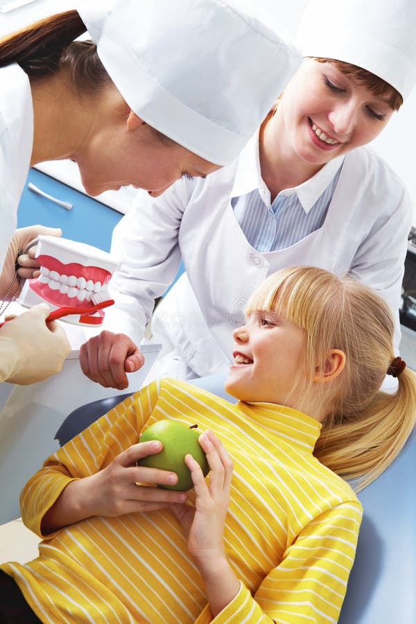 Photo of dentist teaching care dental hygiene little girl with assistant near by. Photo of dentist teaching care dental hygiene little girl with assistant near by