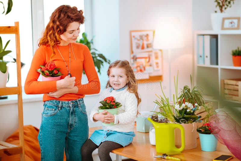 Hija que sostiene las flores que se sientan cerca de la mamá que trabaja en boutique de la flor imagenes de archivo Hija que sostiene las flores que se sientan cerca de la mamá que trabaja en boutique de la flor imagenes de archivo