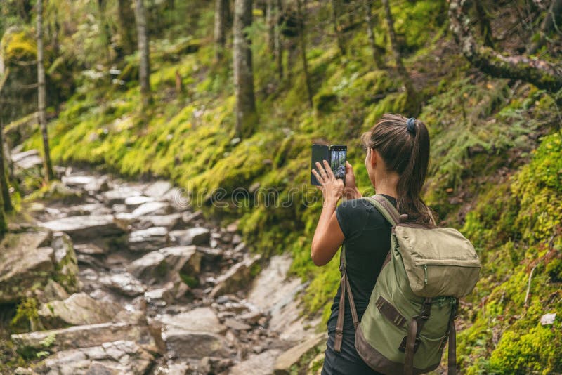 Hiker girl tourist taking picture with mobile phone of trail in nature forest hiking in Quebec outdoors fall autumn season, Canada travel lifestyle. Woman walking with backpack.