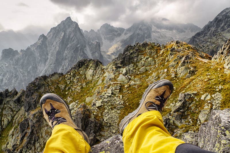 Hiker sitting on the hill and looking on mountains. Hiking boots on legs of tourist