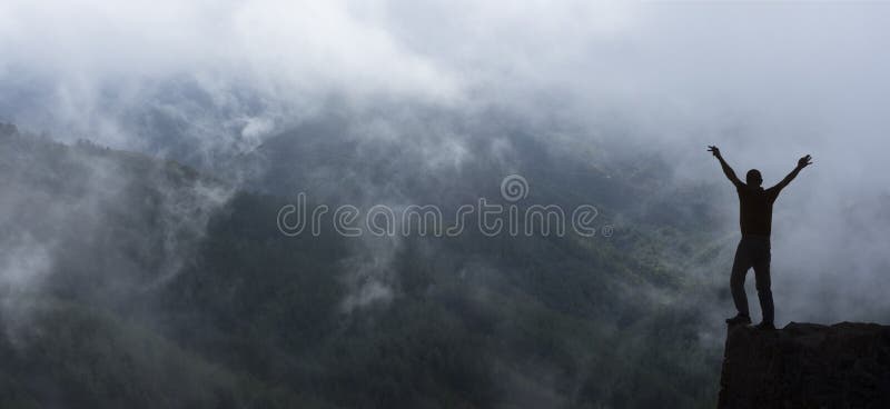 Hiker standing on a cliffs edge. The top of the mountain. Clouds in a light of sunrise.