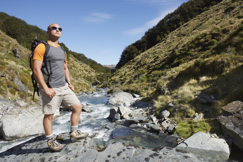 Full length of a male hiker standing by edge of a mountain river. Full length of a male hiker standing by edge of a mountain river
