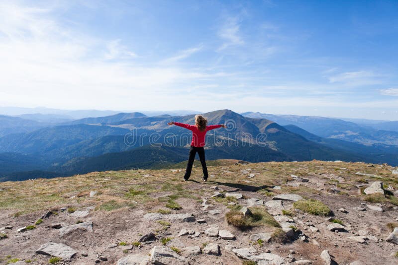 Hiker woman standing on mountain edge and looking to a sky with raised hands embracing vitality freedom. Position back to us. Hiker woman standing on mountain edge and looking to a sky with raised hands embracing vitality freedom. Position back to us