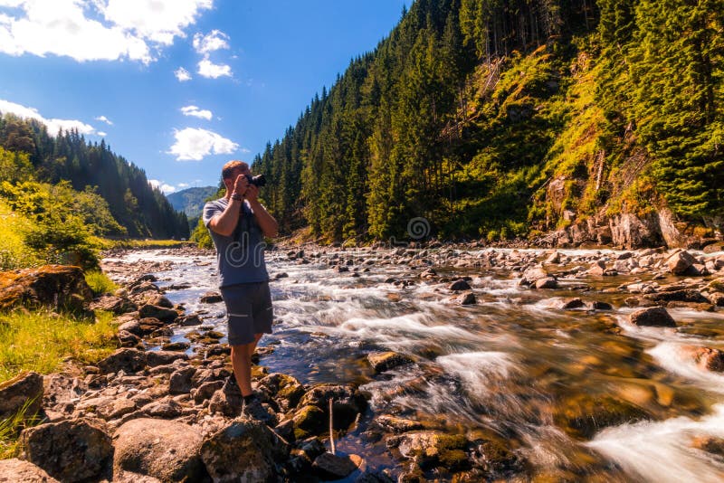 Hiker stops on the mountain river bank to take a picture stock photography Hiker stops on the mountain river bank to take a picture stock photography
