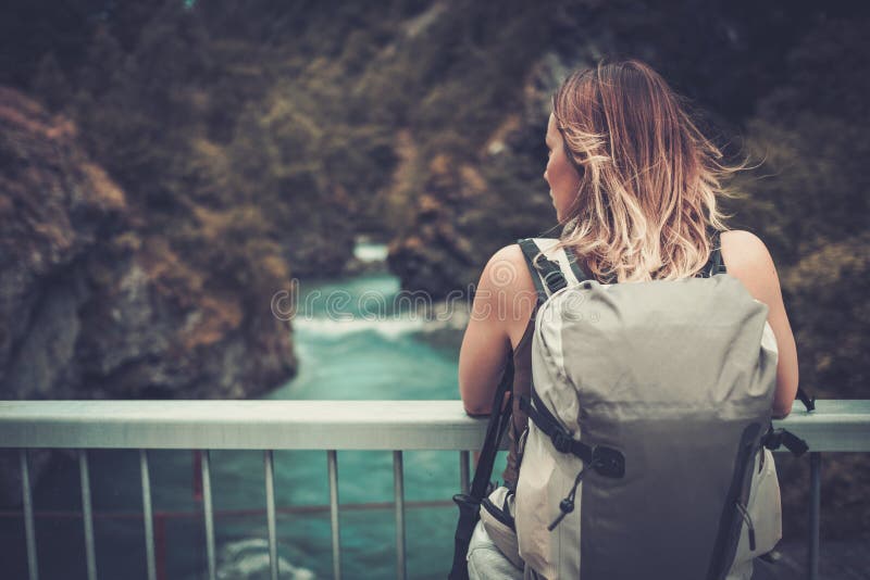 Hiker женщины при рюкзак стоя на мосте над одичалым рекой горы стоковое фото rf