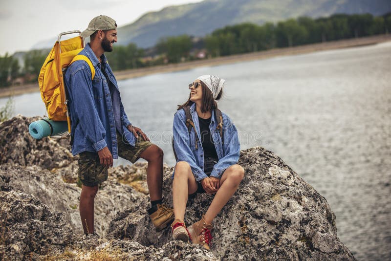 Hikers with Backpacks Sitting on Cliff Enjoying at the Mountain Lake