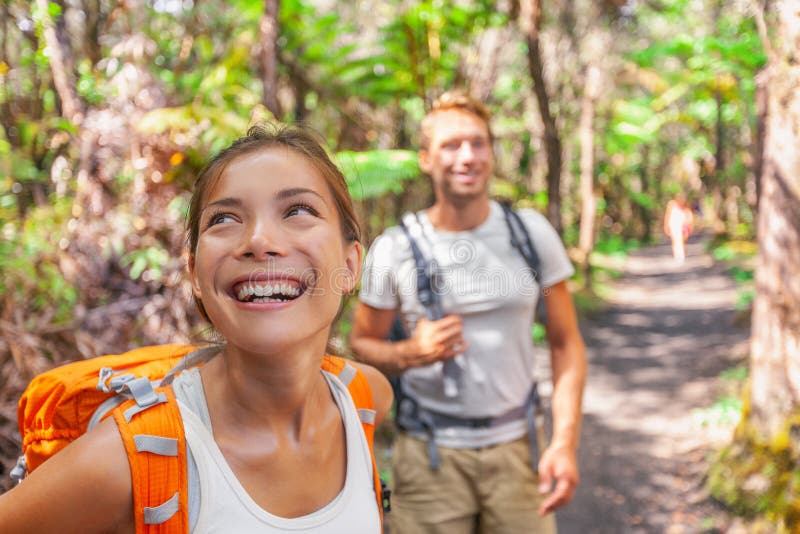 Hiking couple on travel hike outdoor trekking - young active people lifestyle camping with bags in forest. Smiling happy Asian