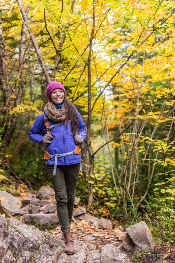 Hiking hiker girl with backpack walking on forest trail in mountains. Asian woman on autumn nature hike with backpack hat and jacket on fall adventure travel outdoors enjoying good weather