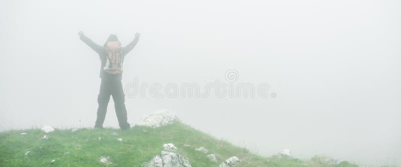 Hiking man with backpack open arms on foggy mountain peak