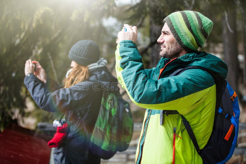 Hiking and photography. Two people taking a picture. Two young people, a men and a woman, with clothing hiking with backpack, taking a picture with a cell phone. Excursions and leisure concept. Preserve the memory of a holiday with photography. Focus on man.