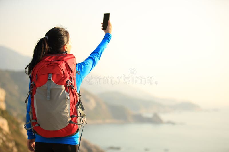 Hiking woman use smart phone taking photo at seaside mountain