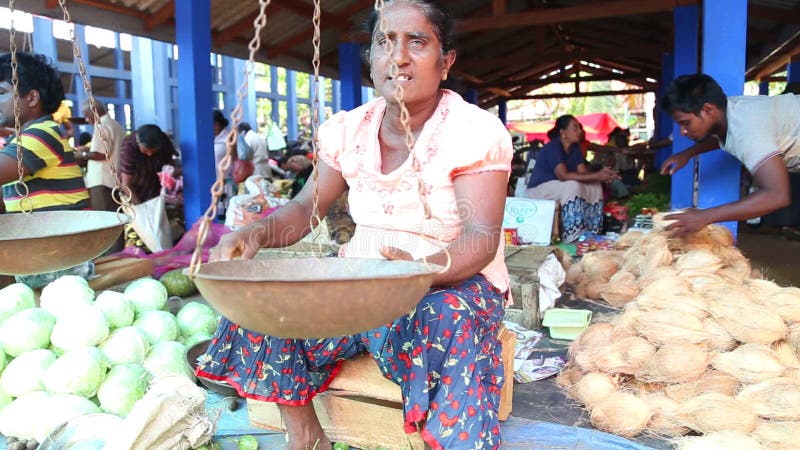 HIKKADUWA, ШРИ-ЛАНКА - МАРТ 2014: Местная женщина сидя перед его масштабом продавая на известном рынке Hikkaduwa воскресенья, для