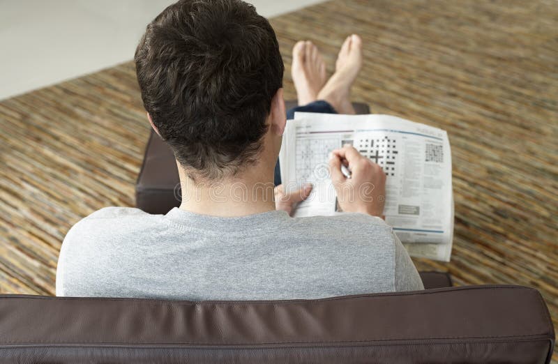 Hintere Ansicht des Mannes Kreuzworträtsel in der Zeitung tuend stockfotografie Hintere Ansicht des Mannes Kreuzworträtsel in der Zeitung tuend stockfotografie