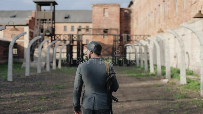 Hintere Ansicht eines deutschen Soldaten mit einem Gewehrmarschieren Vernichtungslager auf dem Hintergrund WWII-Rekonstruktion