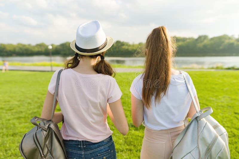 Hintere Ansicht, Freundinnen gehen in den Park in der Natur Mädchen gehen entlang den grünen Rasen, sprechen, haben Spaß stockfotografie Hintere Ansicht, Freundinnen gehen in den Park in der Natur Mädchen gehen entlang den grünen Rasen, sprechen, haben Spaß stockfotografie